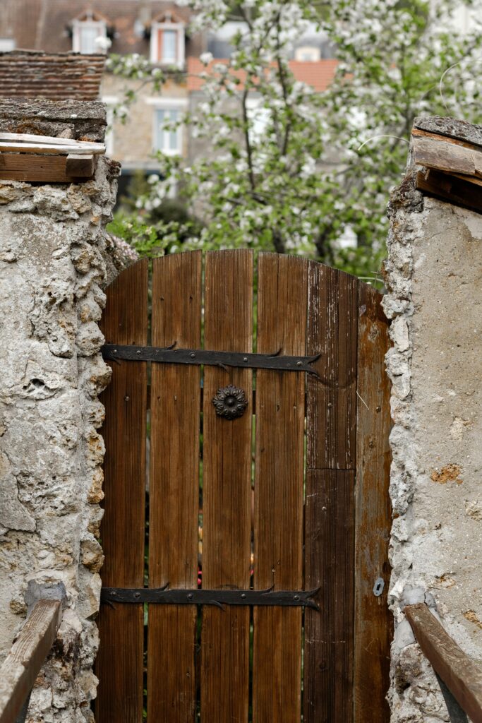 A rustic wooden gate set in a stone wall, with leafy branches peeking through.